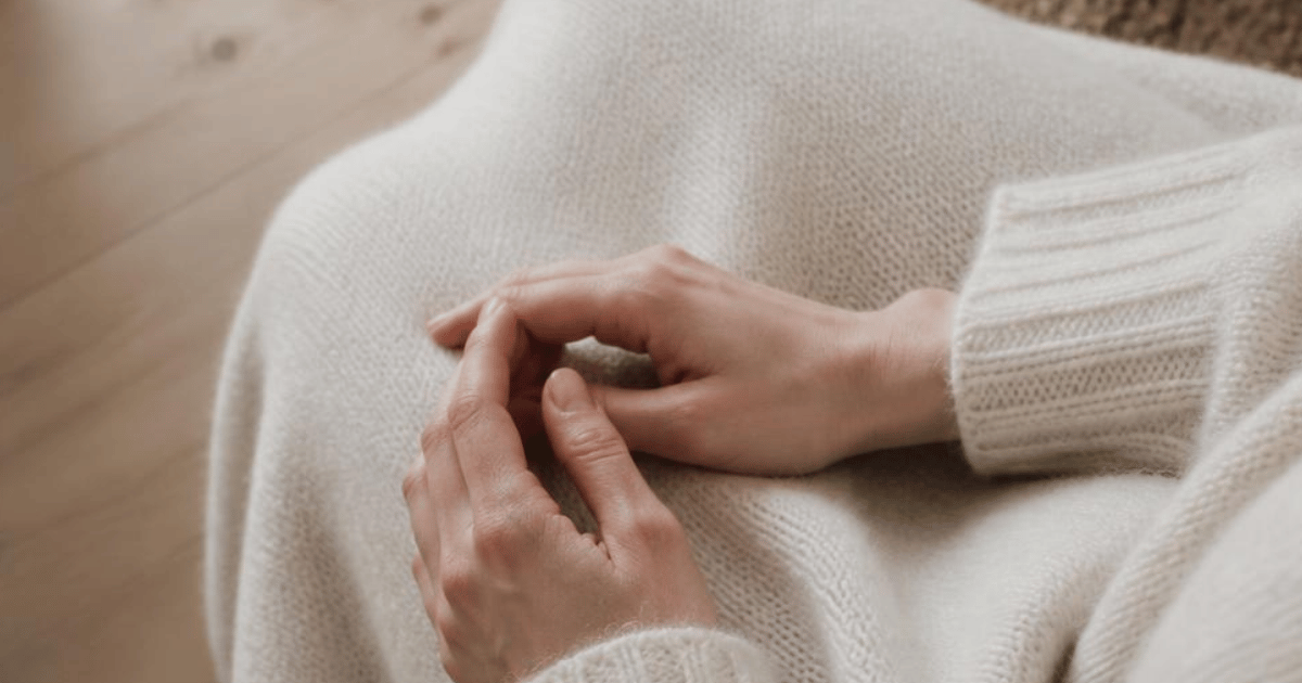 Hænder, der hviler i skødet i en creme sweater