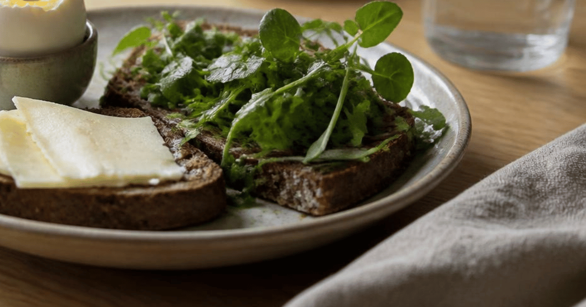 Rugbrød med æg og salat på en tallerken ved et vindue